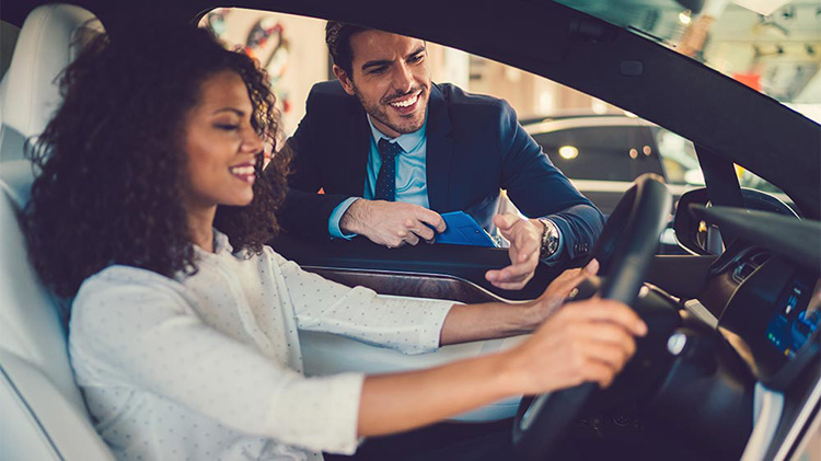 Una mujer pensando en comprar un carro mientras el vendedor se apoya en la ventana.